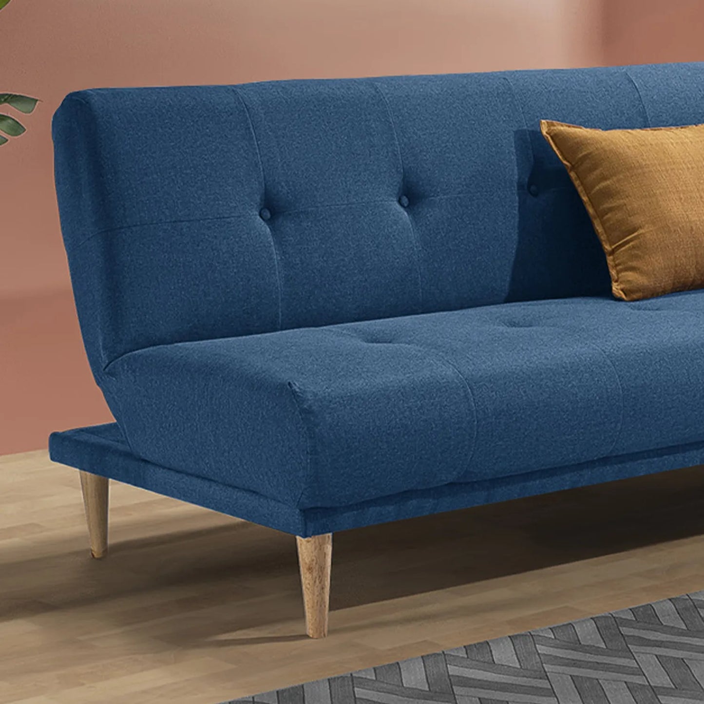 Sofá cama Arena en tela azul con cojín ocre y patas en madera tono natural, encuadre a detalle, ubicado en sala moderna con pared color salmón, ideal para apartamentos y casas de familias colombianas - All Star Muebles Colombia